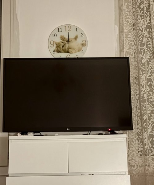 A turned off tv. Over it, a stopped clock with showing a cat.